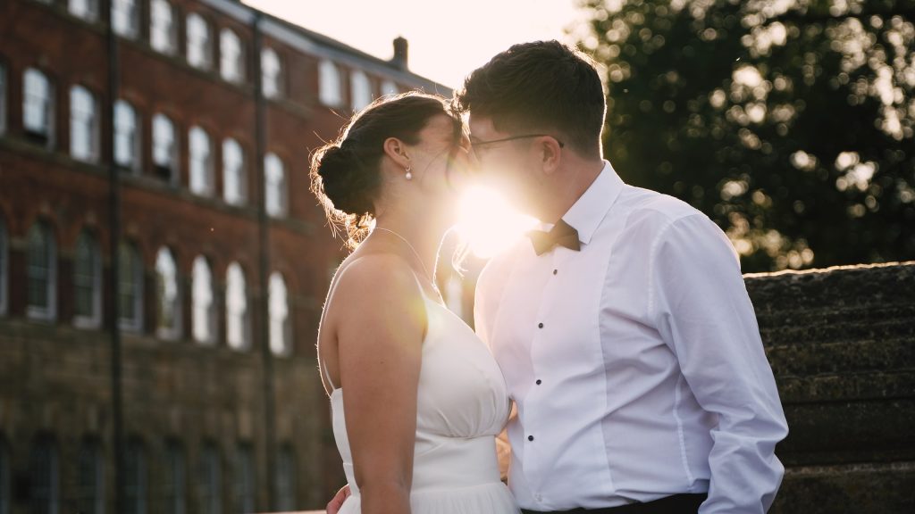 Couple sharing a kiss in golden backlight in front of a red-brick building